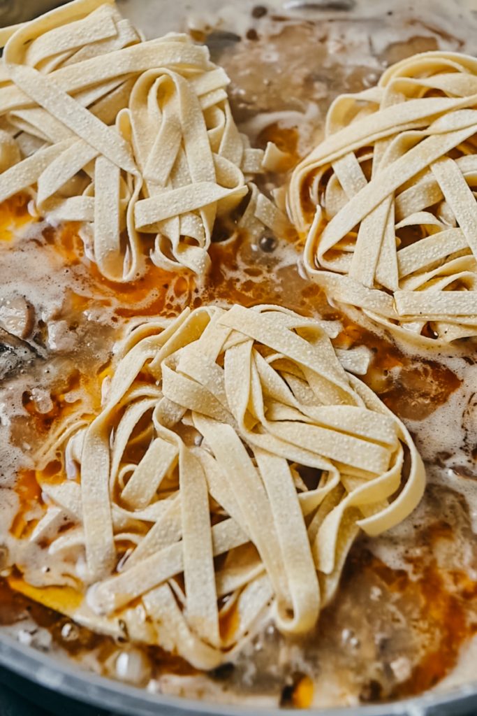 Tagliatelle nests added to the veal stroganoff in a skillet.