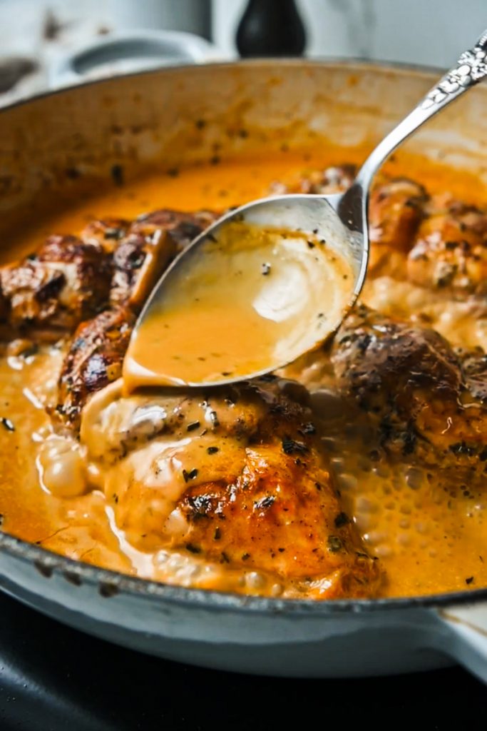 Spooning the braising sauce over the rabbit in a skillet.