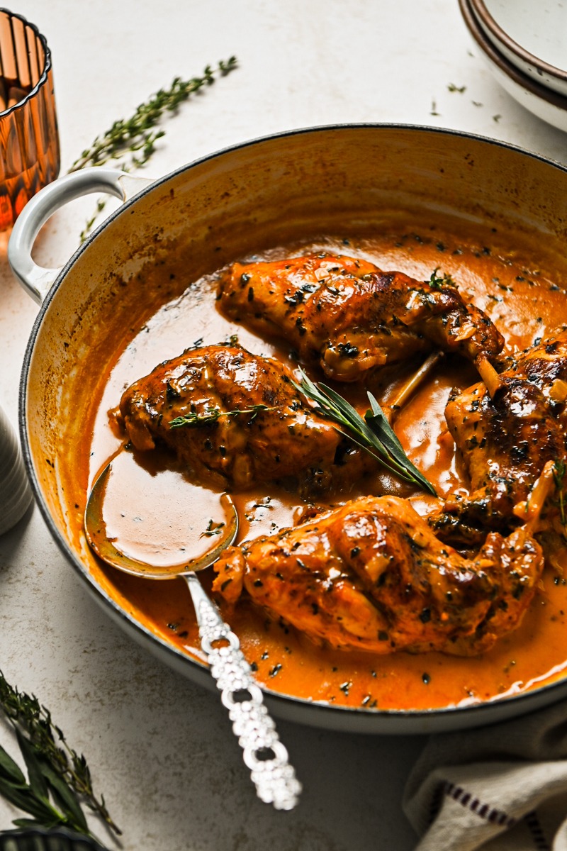 Side view of lapin au vinaigre in a skillet with a serving spoon.