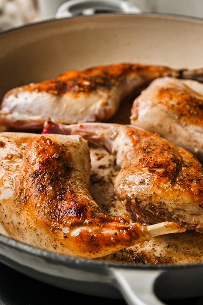 Seared rabbit hind quarters in a skillet.