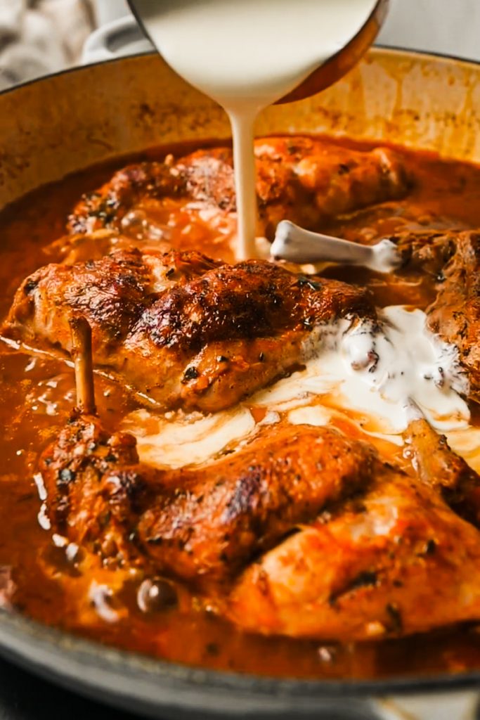 Adding heavy cream to the braised rabbit in a skillet.