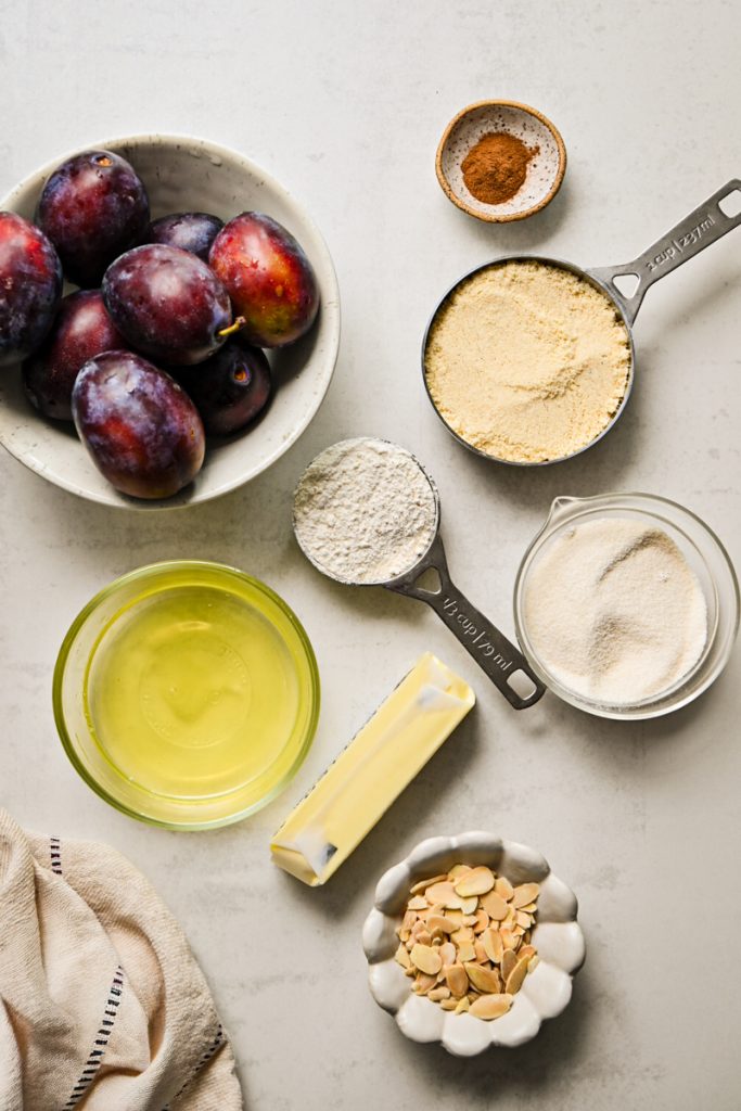 Ingredients for Plum Almond Cake laid out on a countertop, including plums, almond flour, butter, and sliced almonds.