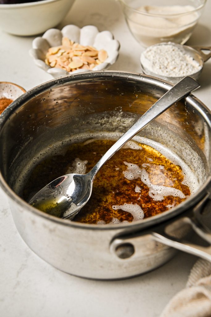 Melted brown butter in a saucepan with a spoon, showing golden milk solids.