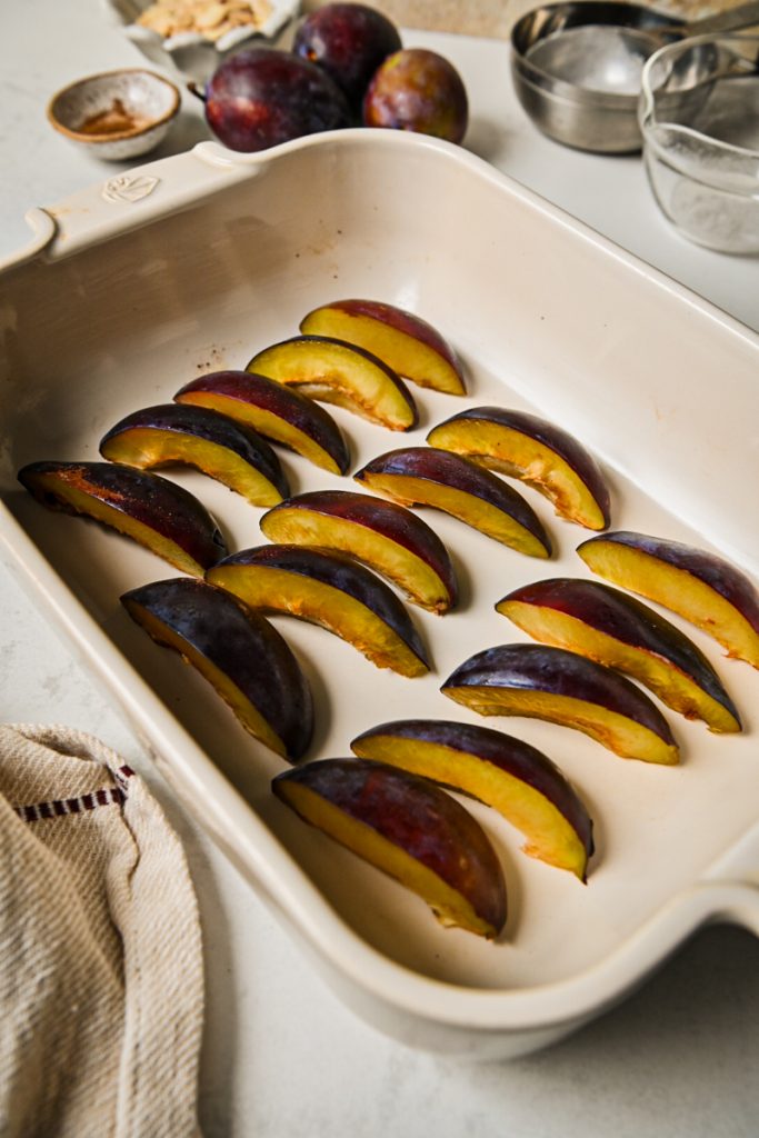Sliced plums arranged in an even layer in a white baking dish.