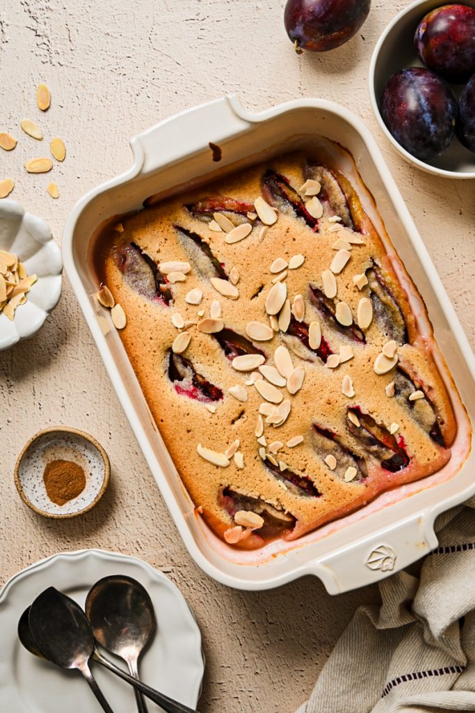 Baked Plum Almond Cake in a white dish topped with sliced almonds.