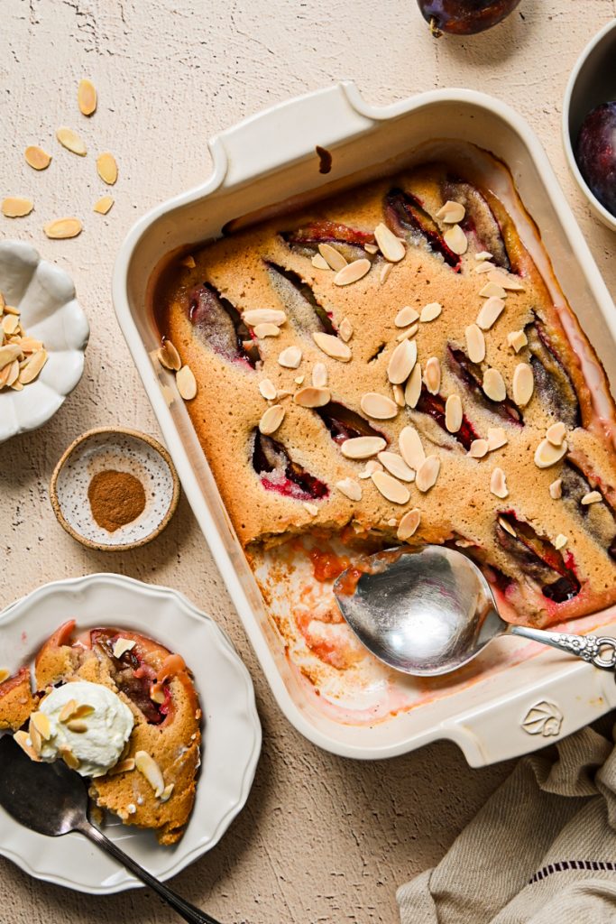Overhead view of the baked Plum Almond Cake in a white baking dish with a serving spoon.