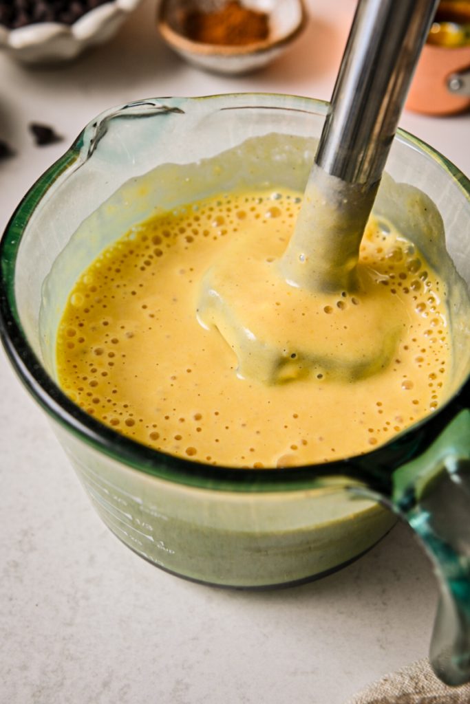 Immersion blender mixing the batter until smooth and pale orange.