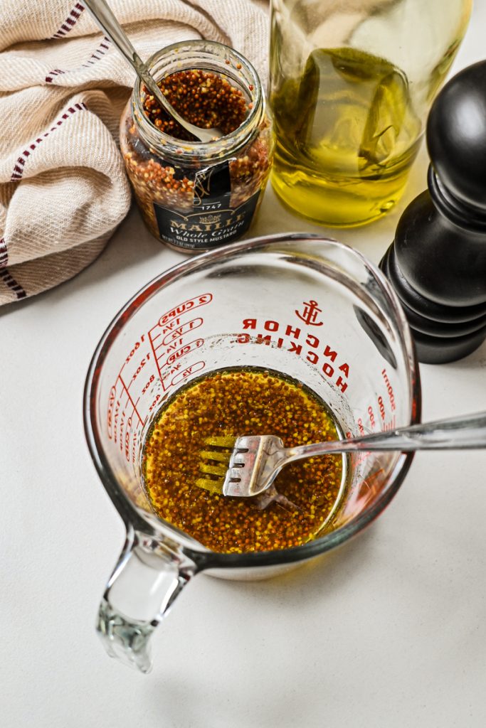 Apple cider vinegar maple mustard marinade whisked together in a glass measuring cup.