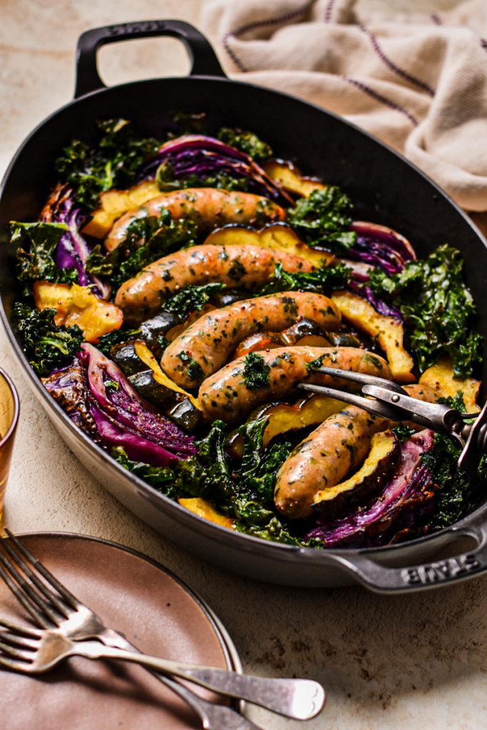 Baked chicken sausages, acorn squash, red cabbage, and kale in a cast iron pan.